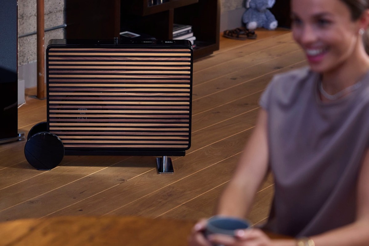 Wood-slatted subwoofer on the floor, near a table with a coffee cup