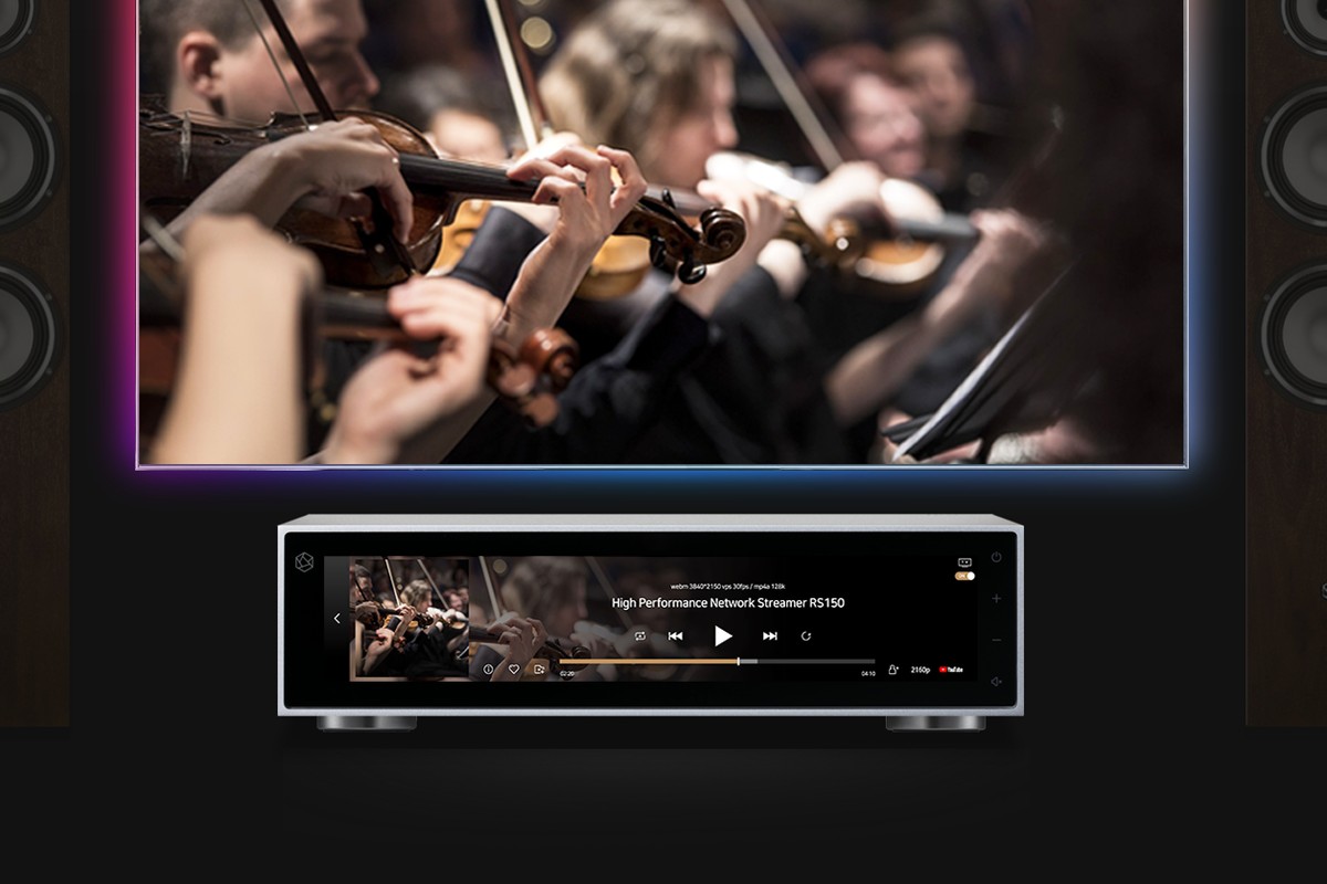 Streamer argent sous un téléviseur affichant un orchestre, entre deux enceintes colonnes