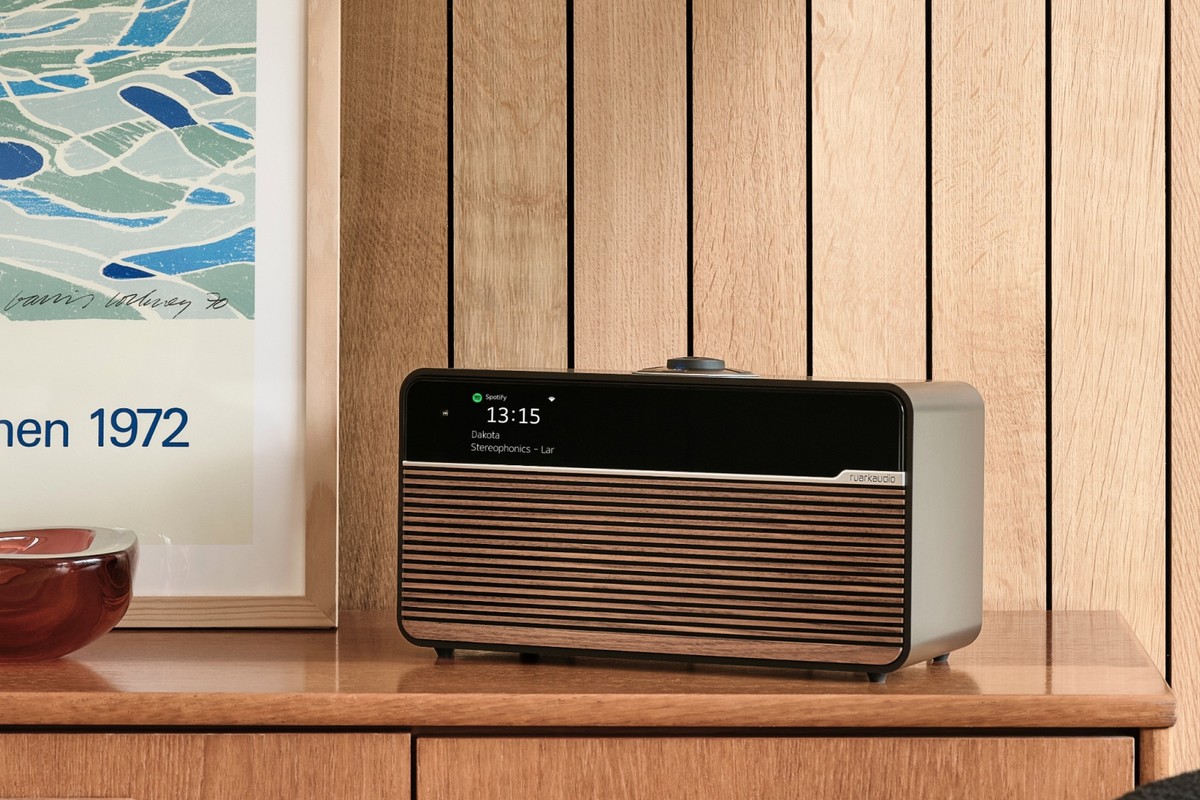 Sistema musicale in finitura Espresso con griglia Walnut su una credenza in legno, davanti a una parete a lamelle di rovere e a un poster incorniciato