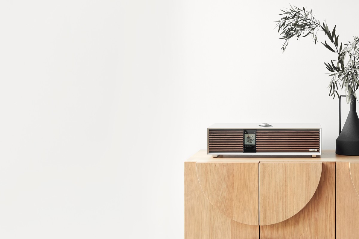 Light grey audio system on an oak sideboard, black vase, large bright wall around it