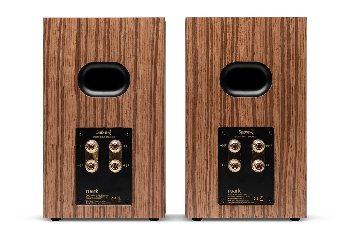 Rear view of a walnut veneer speaker, port and terminals visible, on a white background