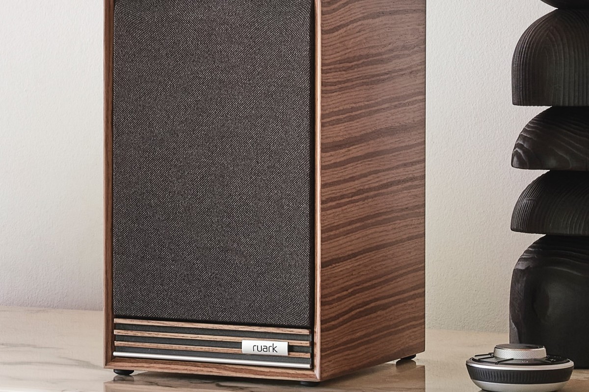 Speaker with walnut veneer, fabric grille and walnut slats, standing on a marble surface