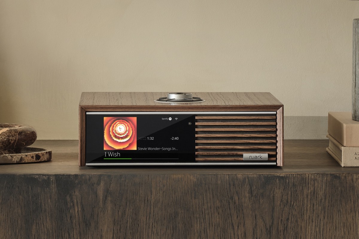 Ruark R610 en noyer Fused Walnut seule sur un meuble sombre, écran allumé