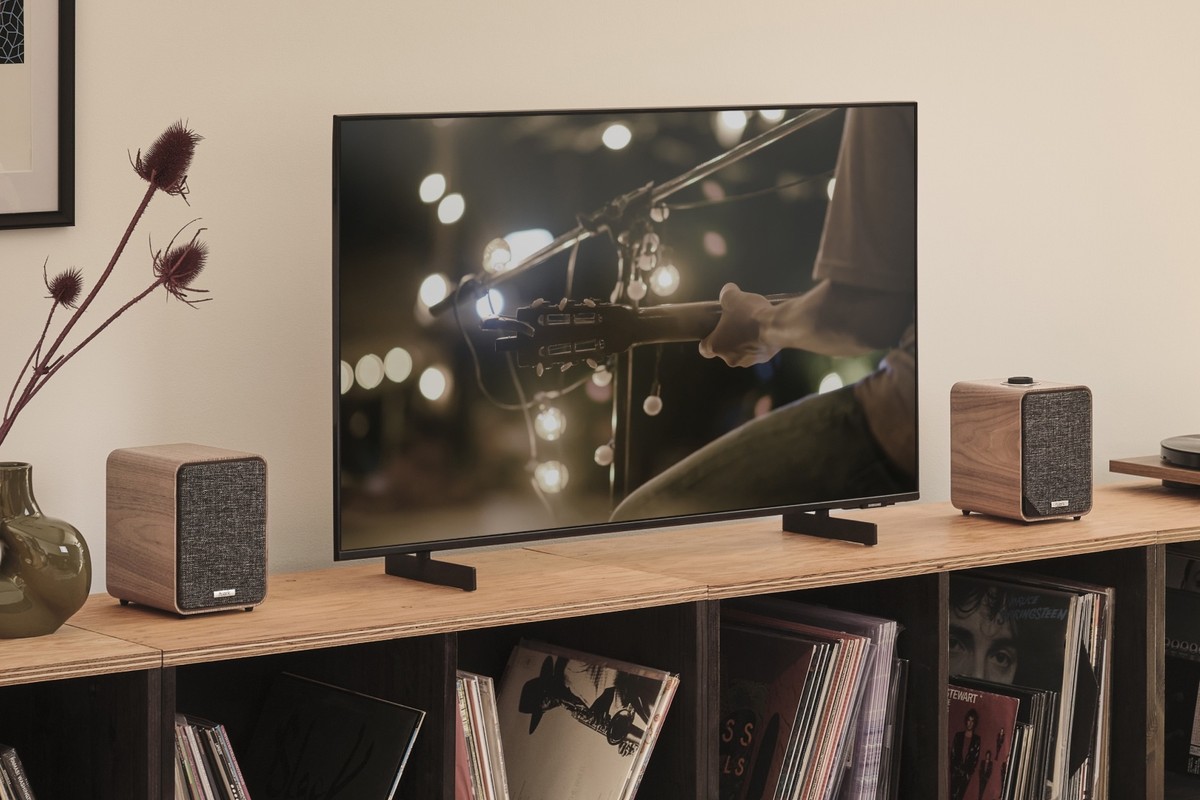 Coppia di diffusori attivi ai lati di un televisore appoggiato su un mobile per vinili in legno