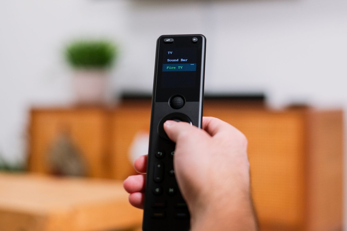 Remote in the foreground in front of a television that is on