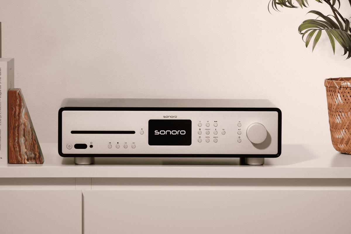 Receiver mit silberner Front auf einem hellen Regal, zwischen Büchern und einer Pflanze
