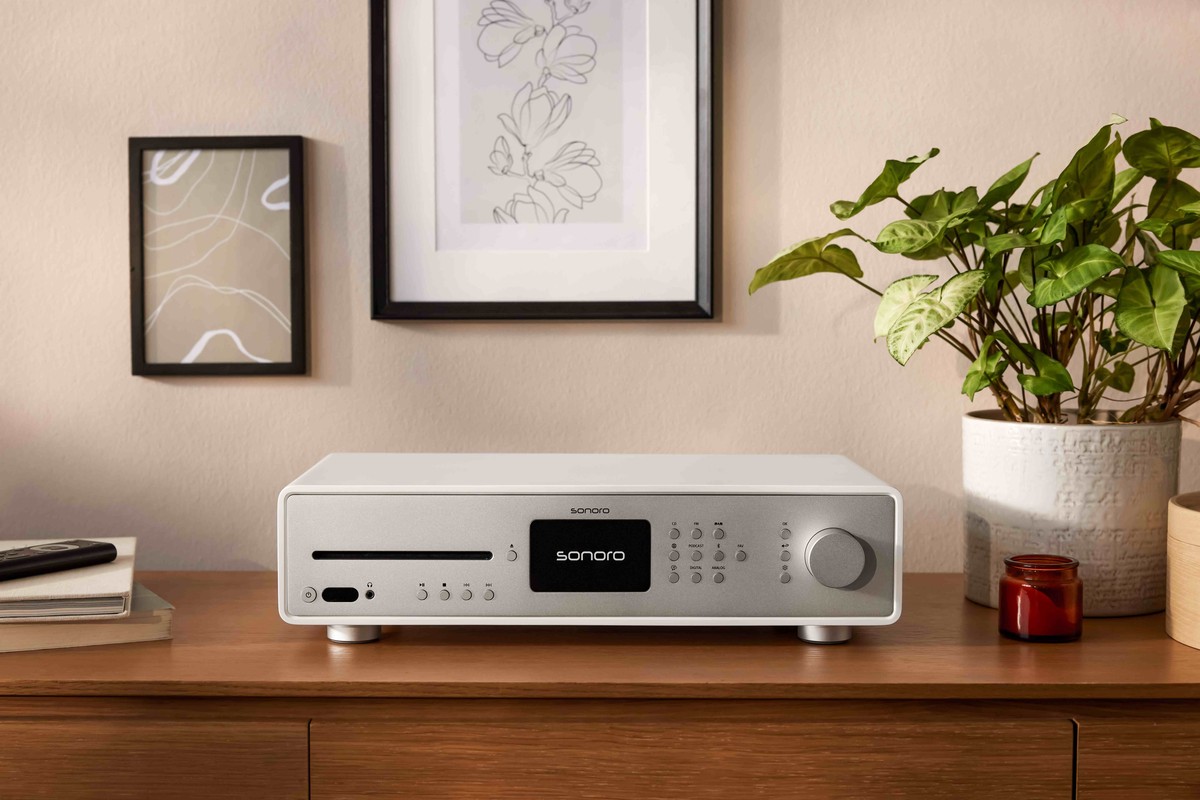 Weisser Receiver auf einer Holzkommode, vor Bilderrahmen und einer Grünpflanze