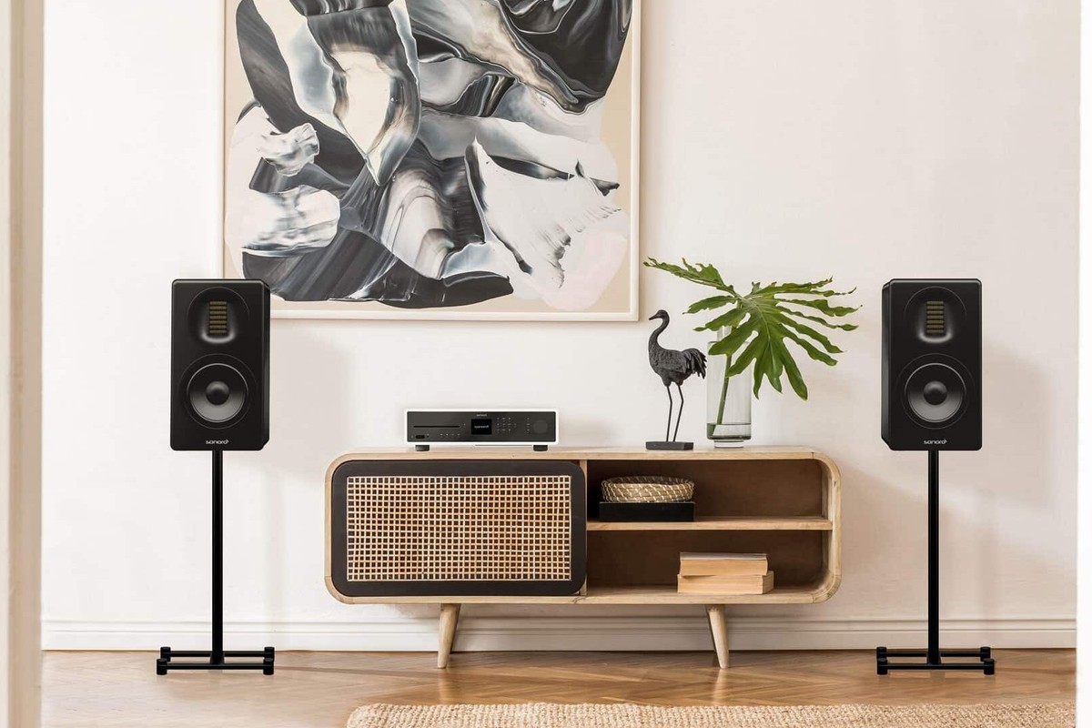 Two black speakers on stands either side of a wood and cane TV cabinet