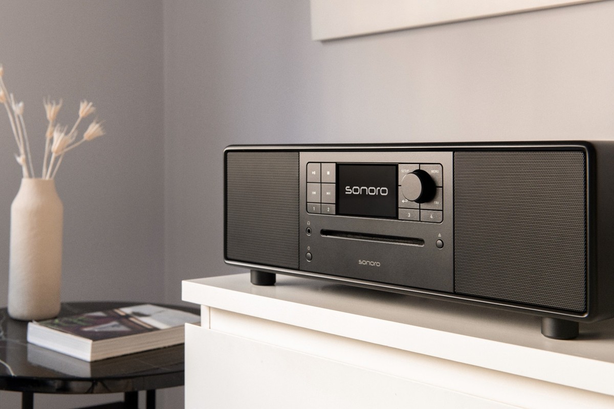Matt black music system on a white cabinet beside a vase of dried flowers