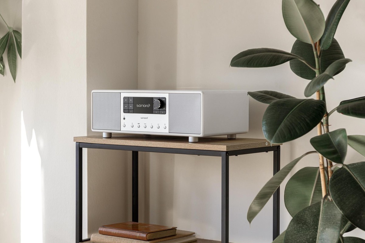 White audio system on a metal and wood console between two green plants