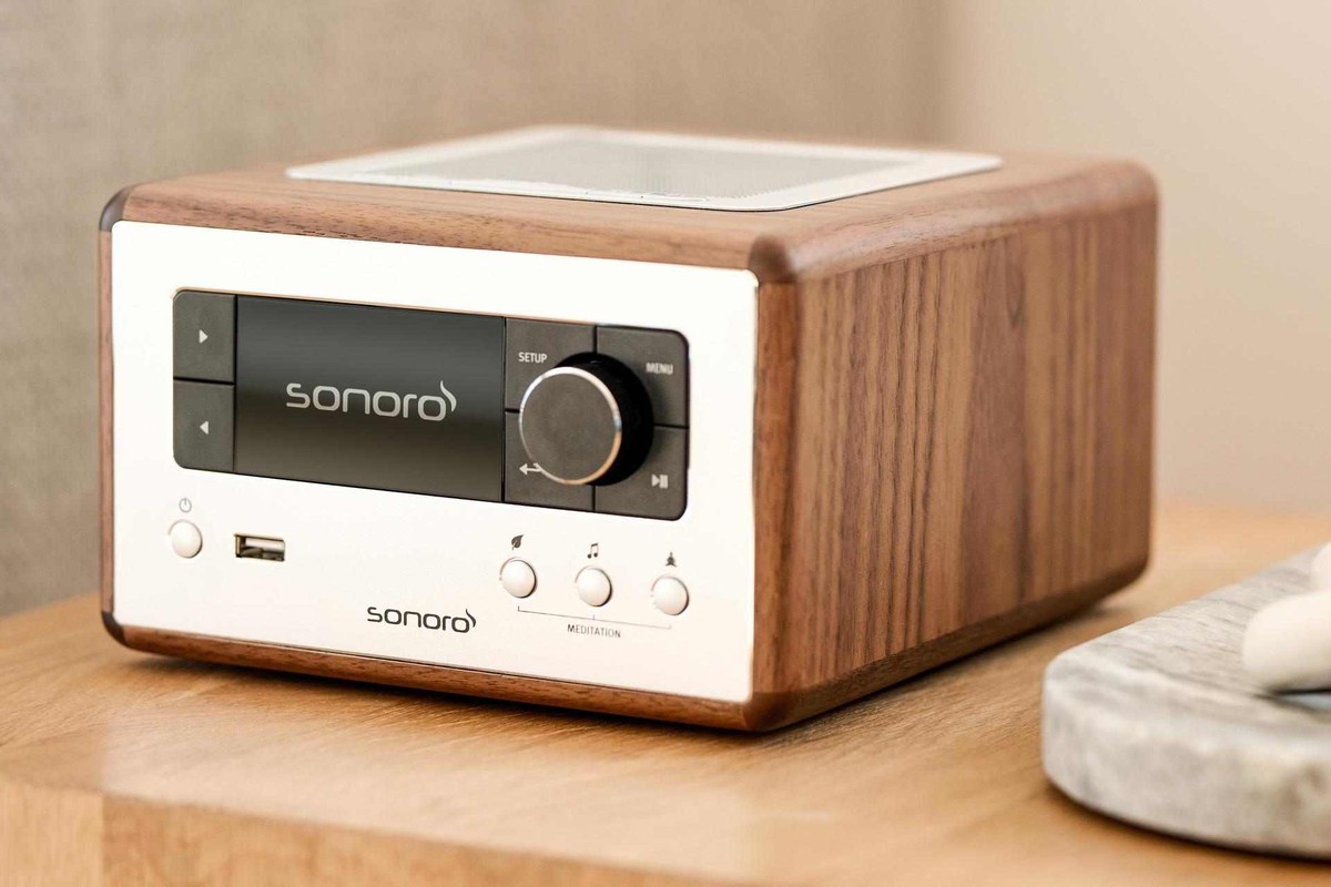 Walnut version on a light wooden bedside table, speaker grille visible on top