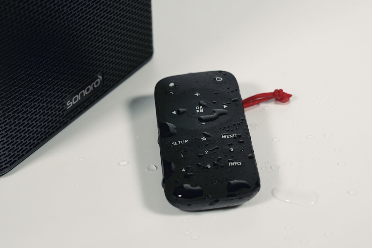 Black remote control covered in water drops, lying next to the radio