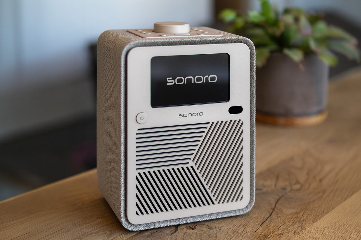 Système audio compact à façade crème et habillage tissu sur un buffet en chêne, plante verte en arrière-plan