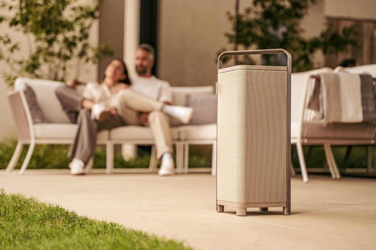 Enceinte nomade beige posée sur une terrasse, couple installé au salon de jardin