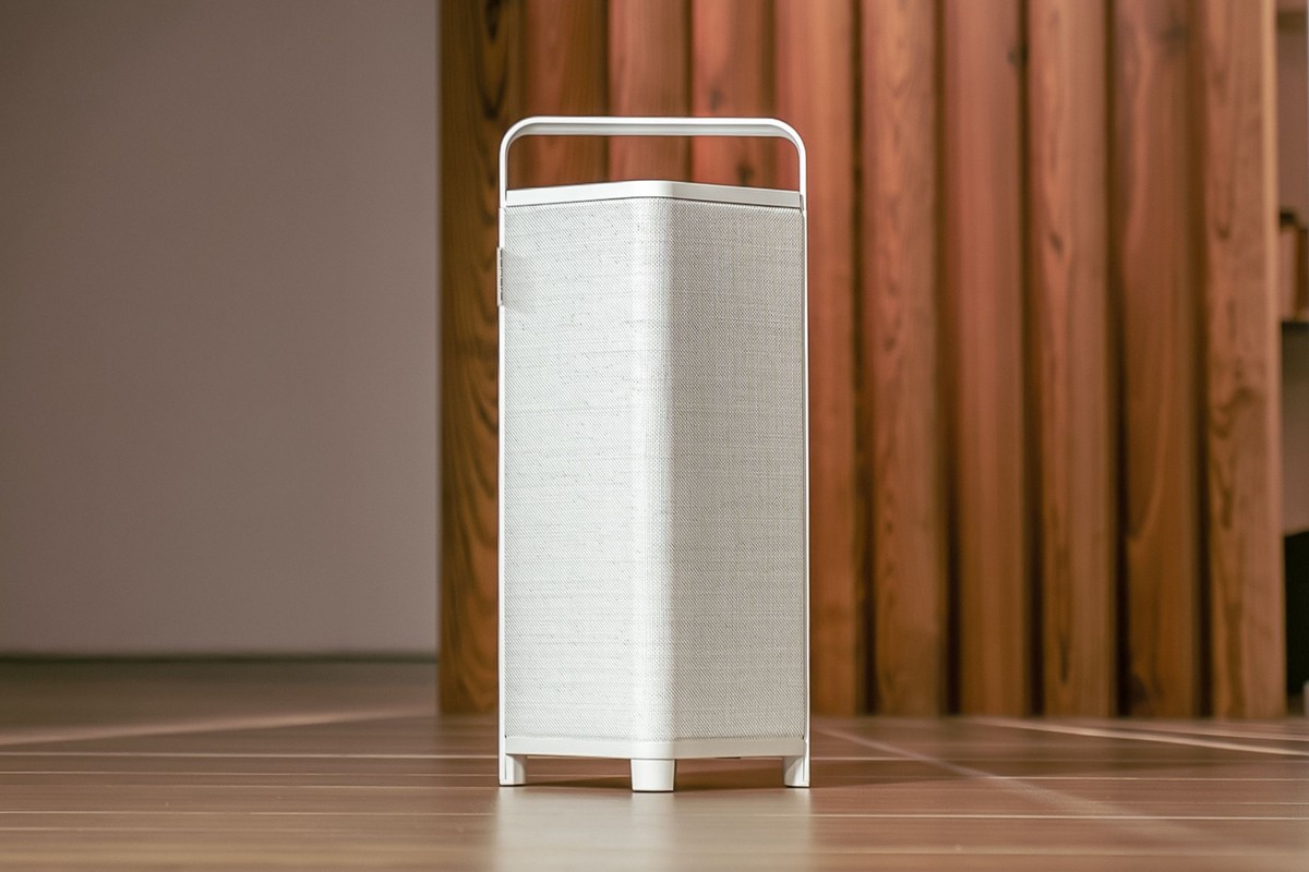 Enceinte blanche à anse en aluminium sur un parquet, devant un mur en lames de bois