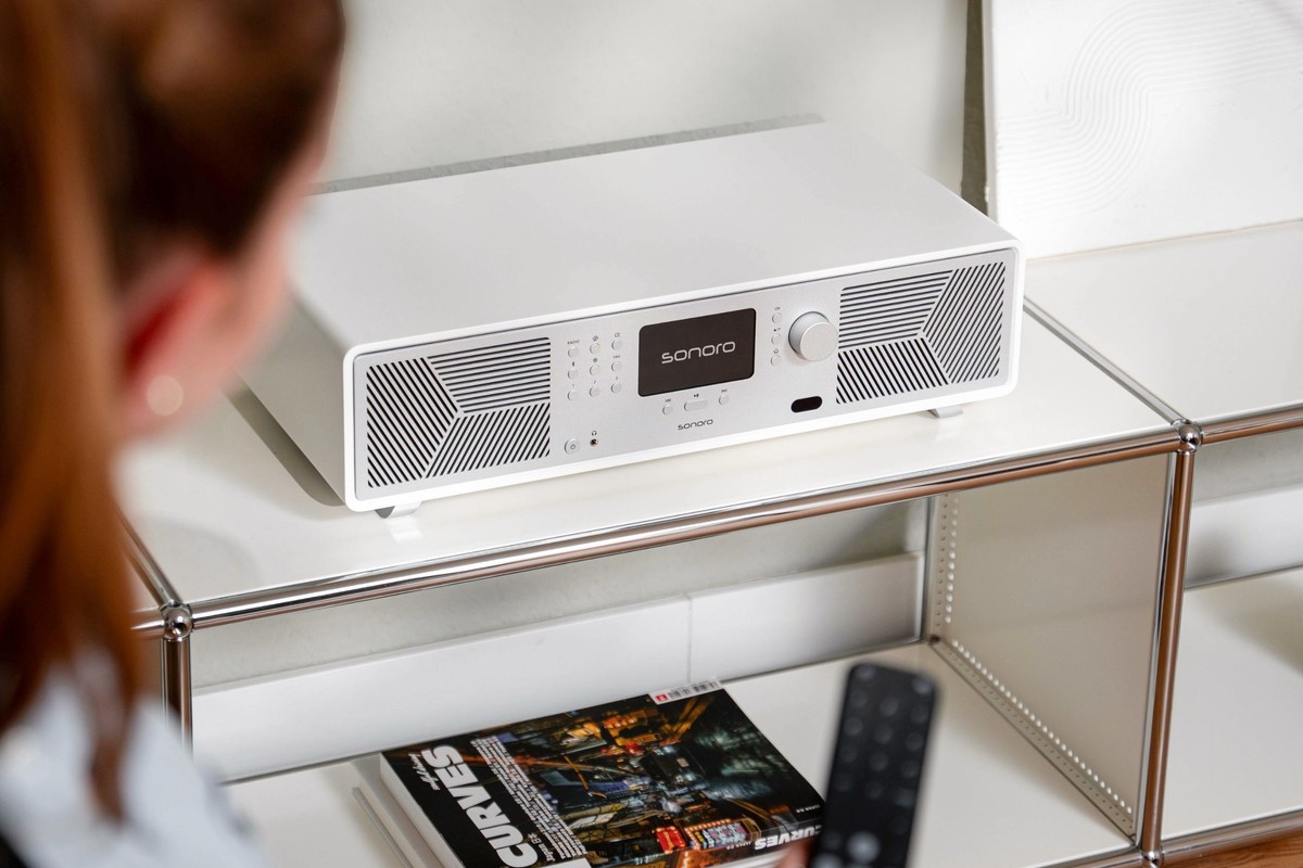 Femme pointant une télécommande vers un système audio blanc posé sur un meuble métallique blanc