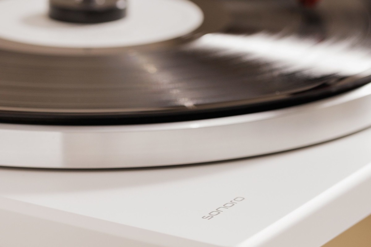 Disque vinyle en rotation sur une platine blanche, bord du plateau en aluminium