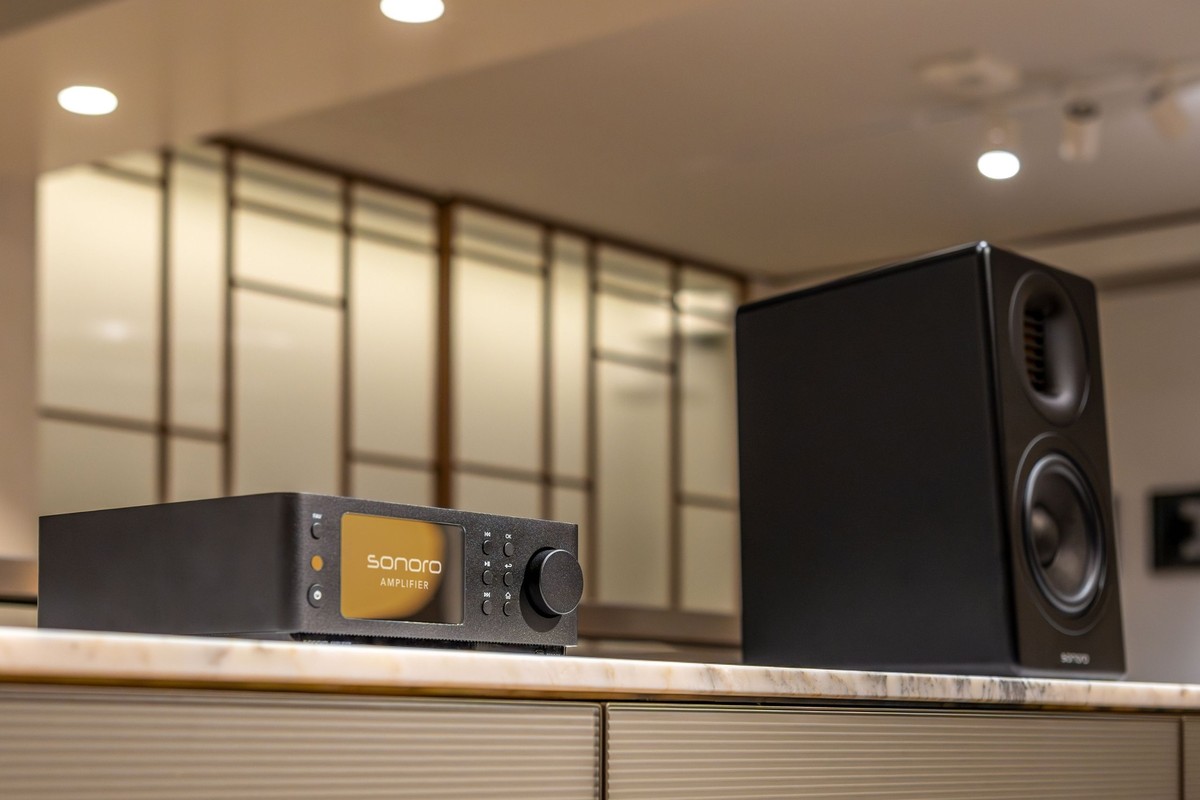 Black amplifier on a marble worktop next to a black bookshelf speaker