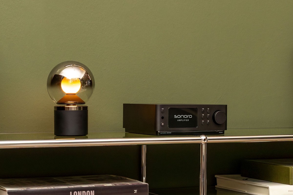 Black streaming amplifier on a chrome shelf beside a mirrored globe lamp
