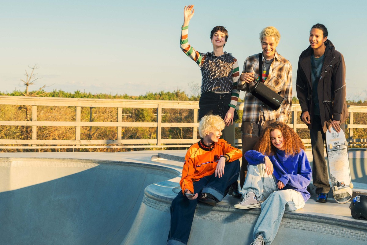 Groupe d'amis dans un skatepark, enceinte portable noire portée en bandoulière