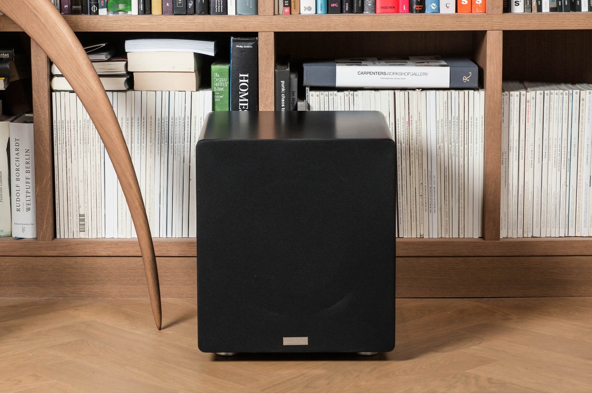 Black subwoofer standing in front of shelving in a living room