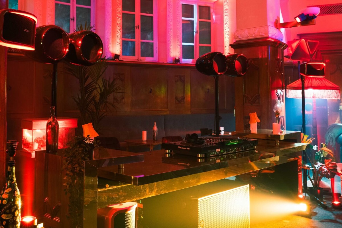 Paires d'enceintes noires sur pied à côté d'une console de DJ dans un salon aux éclairages rouges