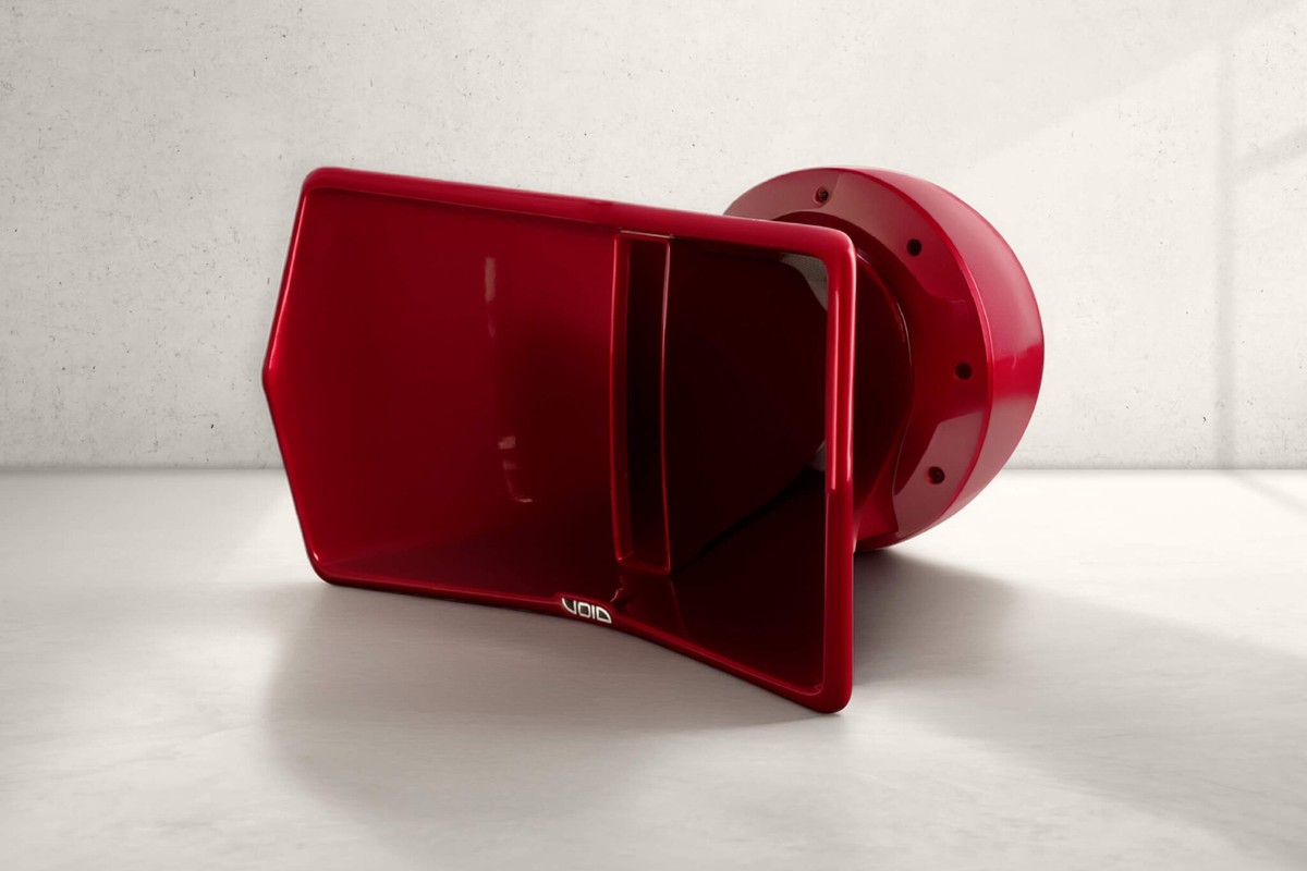 Enceinte rouge à trompe posée sur un sol en béton clair