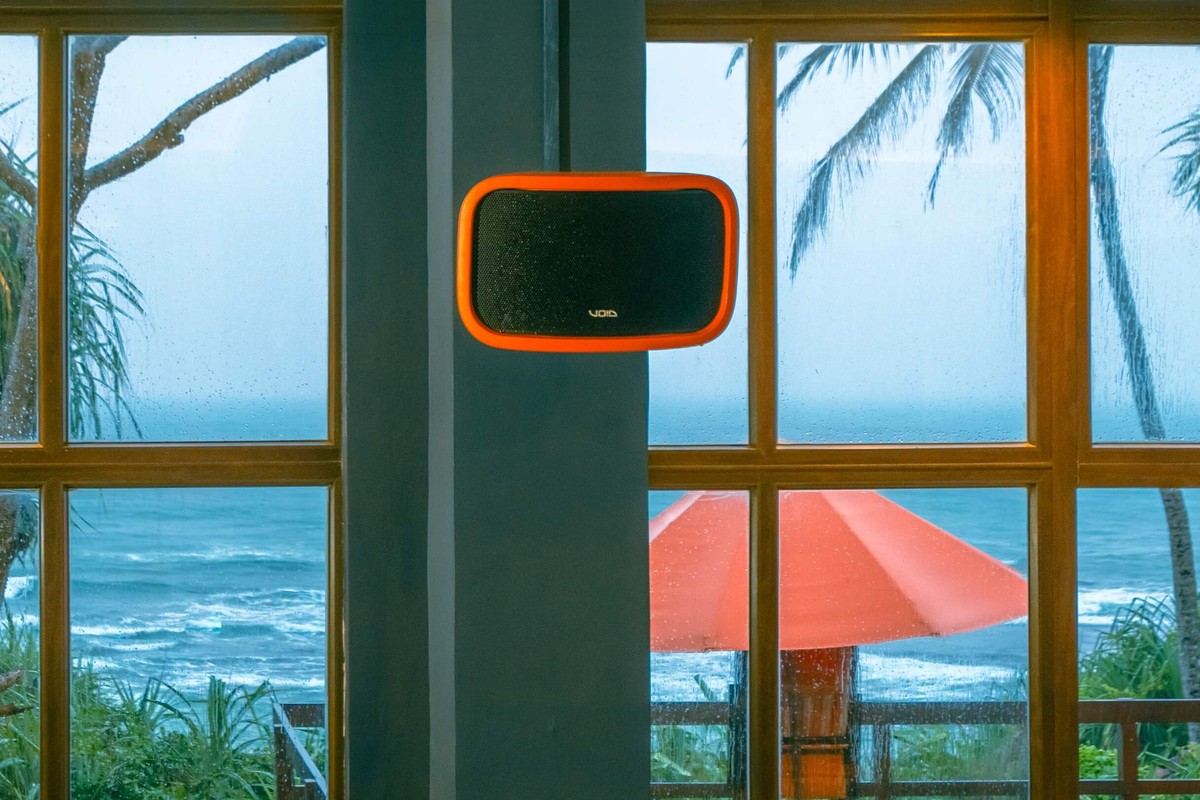 Enceinte dans une finition orange sur mesure, fixée à un poteau devant une baie vitrée face à la mer