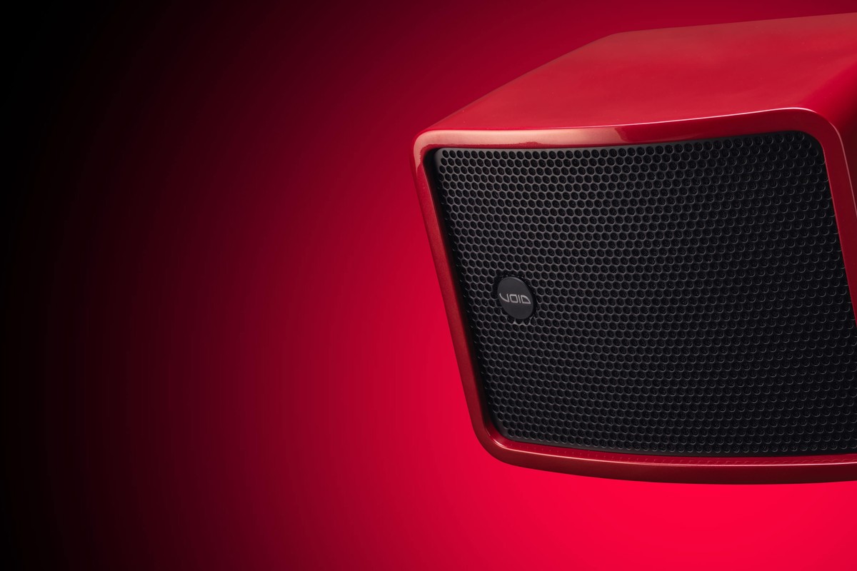Grille perforée noire et logo Void sur le flanc d'un caisson de basses rouge, fond dégradé