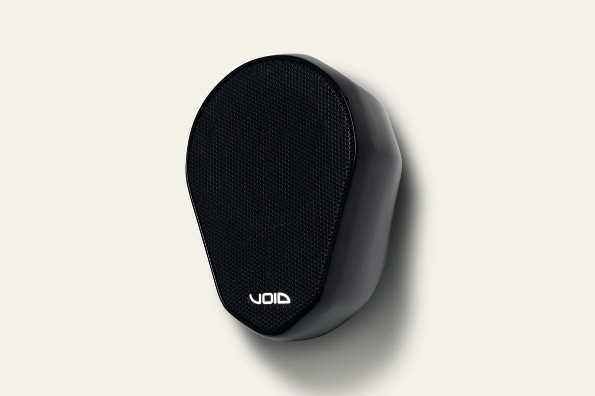 Enceinte noire Void Acoustics Indigo 6s vue de trois quarts, grille perforée et logo, sur fond crème