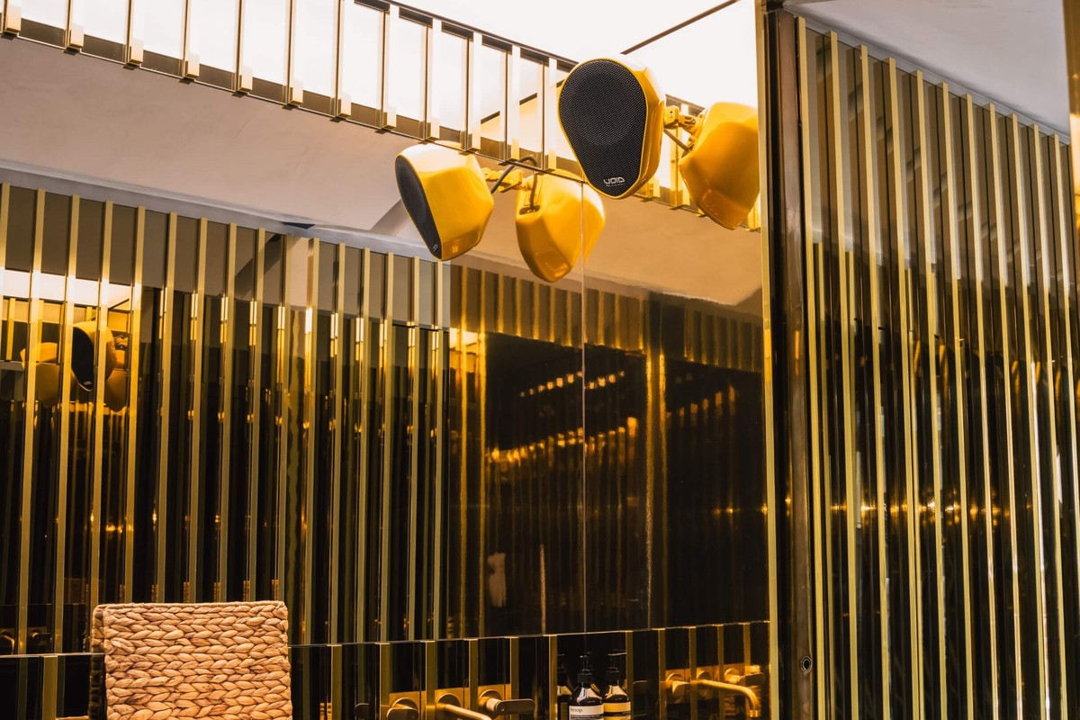 Enceintes jaunes suspendues devant des lames dorées dans un espace de restauration