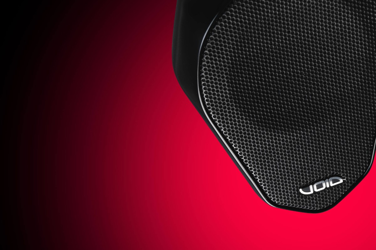 Gros plan sur la grille noire d'une enceinte compacte sur fond rouge dégradé