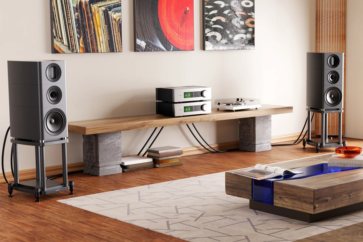 Two speakers on stands in a living room, with a turntable, records and a coffee table