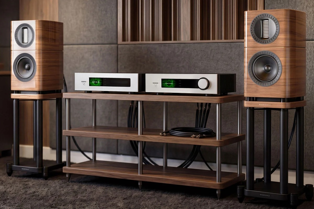 Two light walnut speakers on stands on either side of a cabinet holding two amplifiers