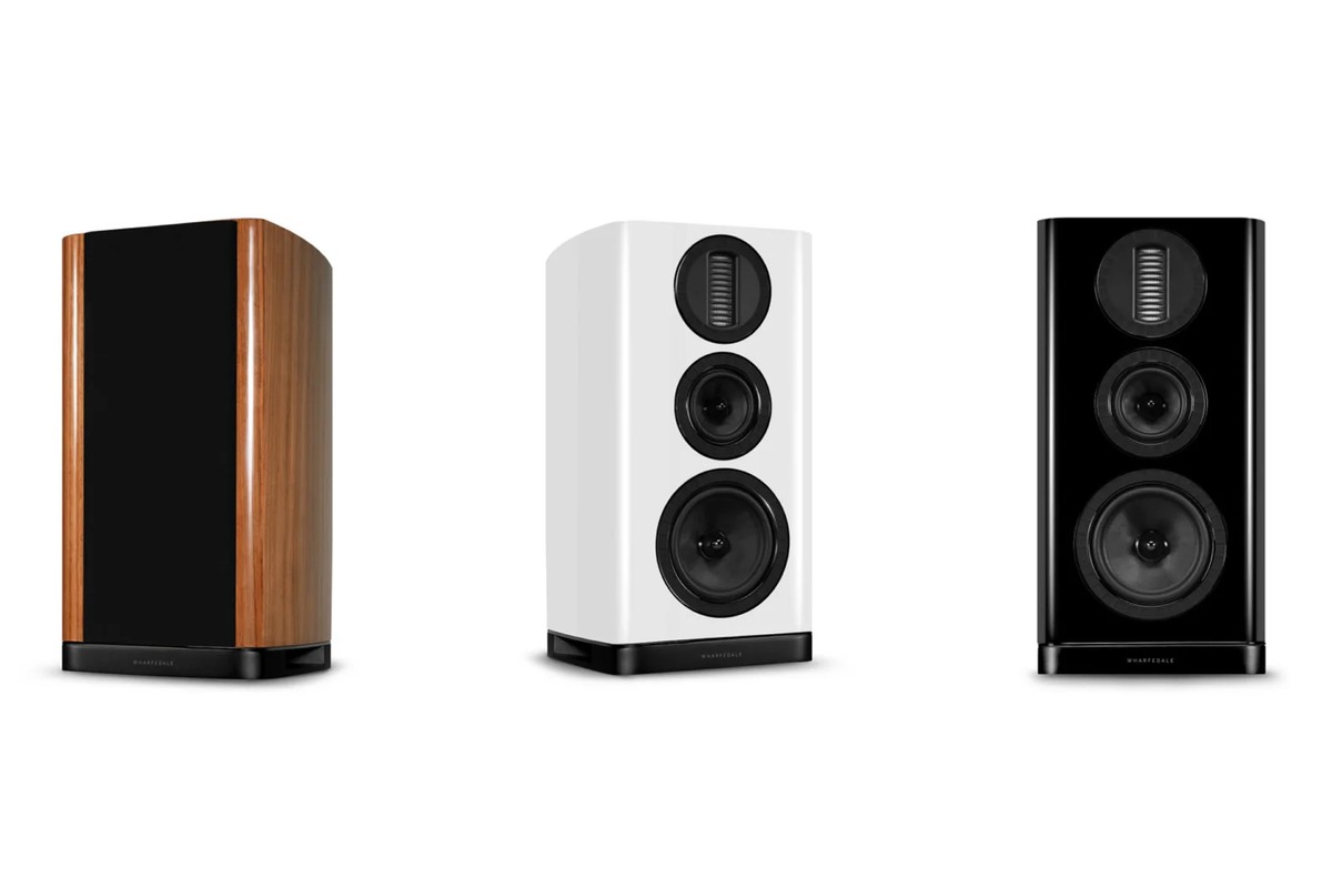 Three bookshelf speakers in walnut, hi-gloss white and hi-gloss black, seen from three-quarter angle on a white background