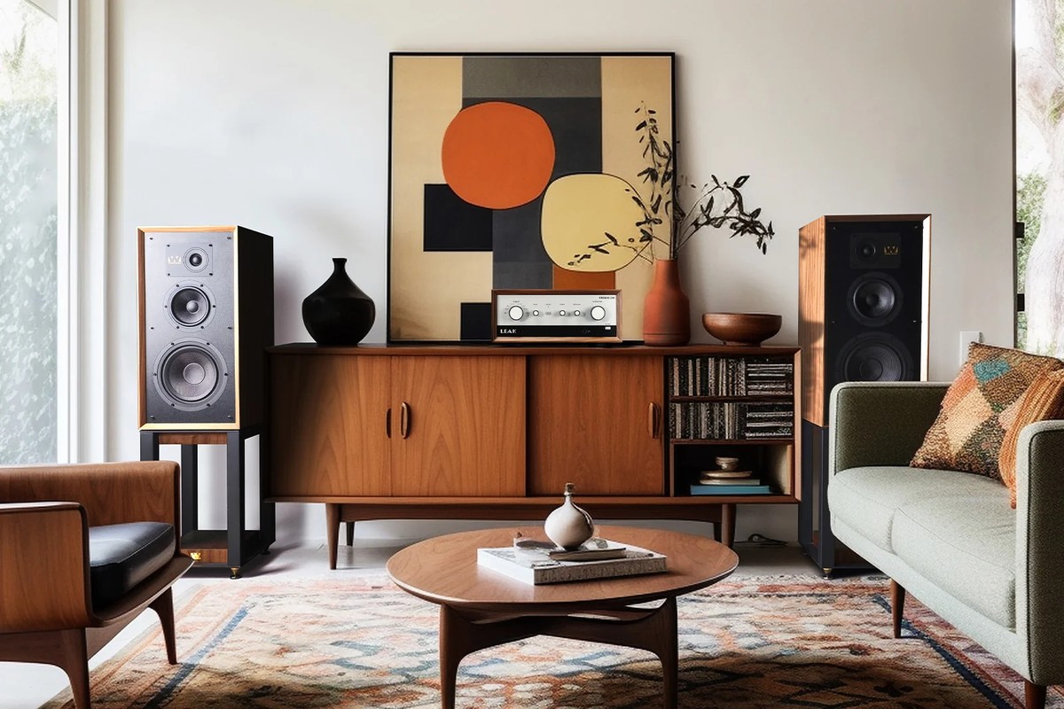 Two stand-mounted speakers in a living room, either side of a low cabinet holding an amplifier