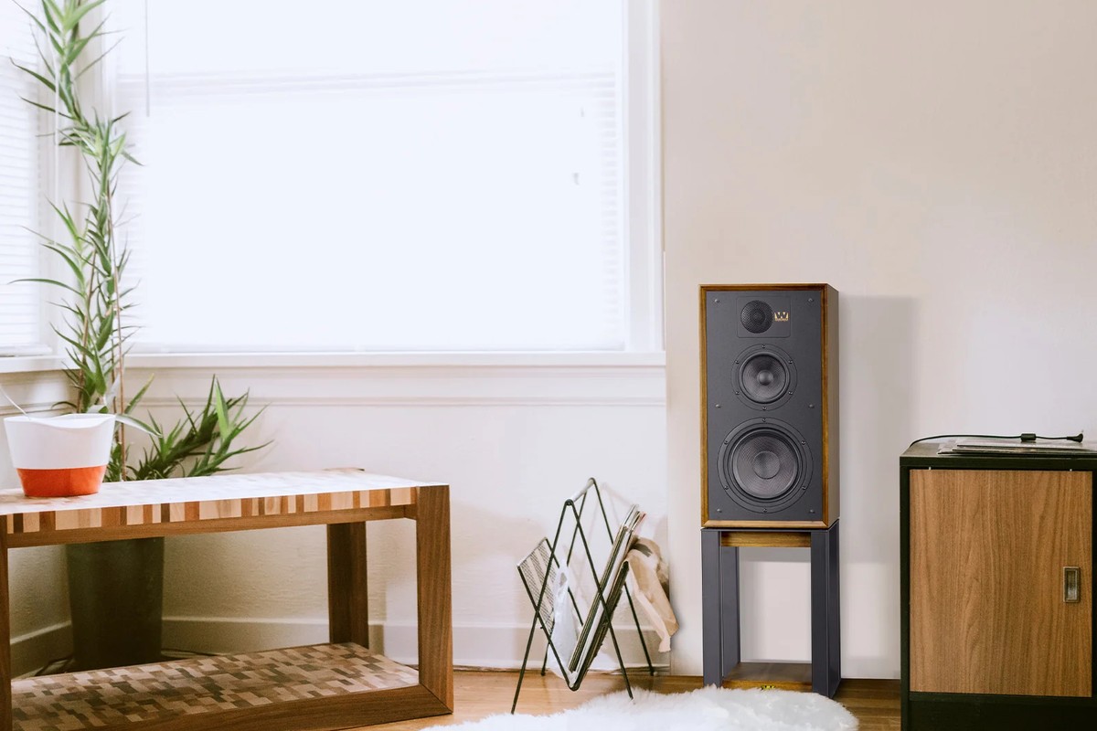 Speaker on a stand in a bright living room, near a coffee table and a magazine rack