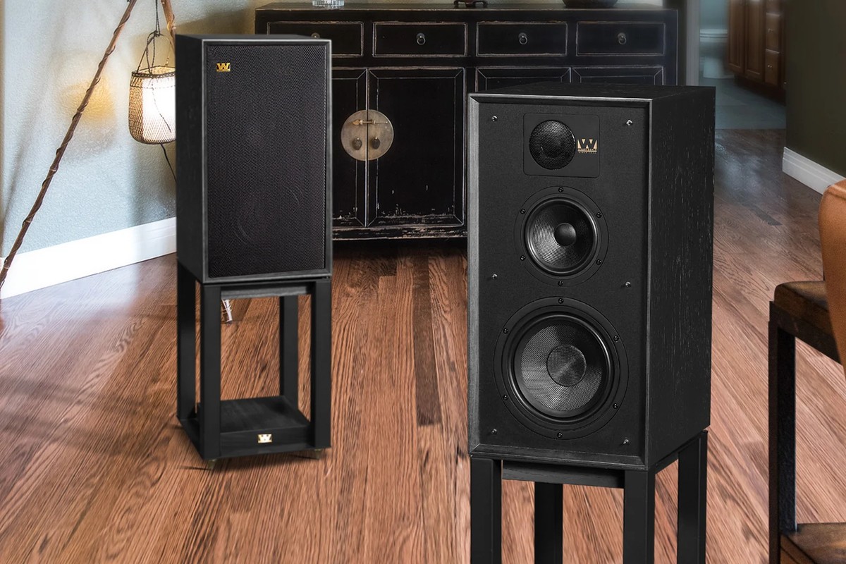 Two black speakers on black stands, standing on a wooden floor