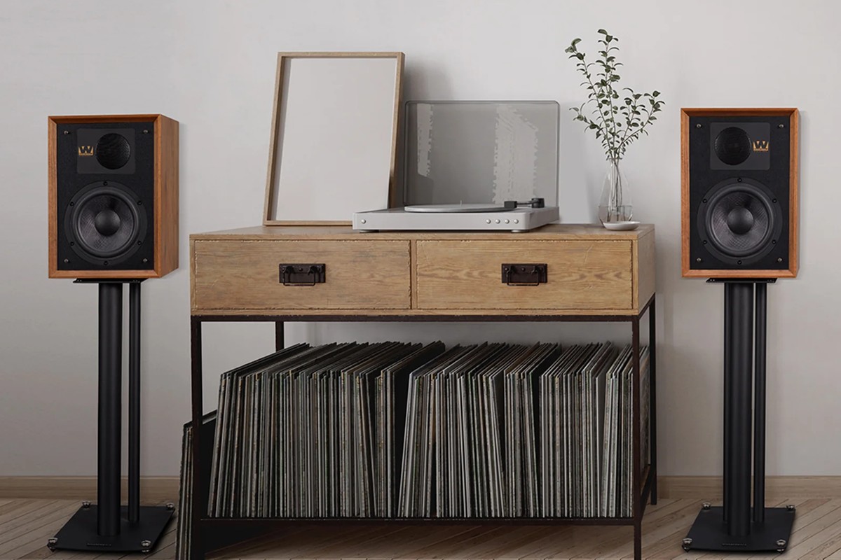 Two mahogany speakers on stands either side of a low cabinet holding a turntable and records