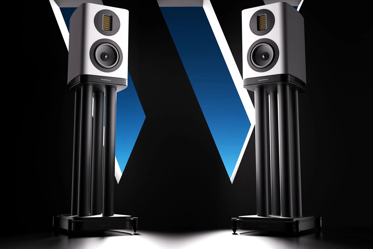 Two white speakers mounted on black stands against a dark background