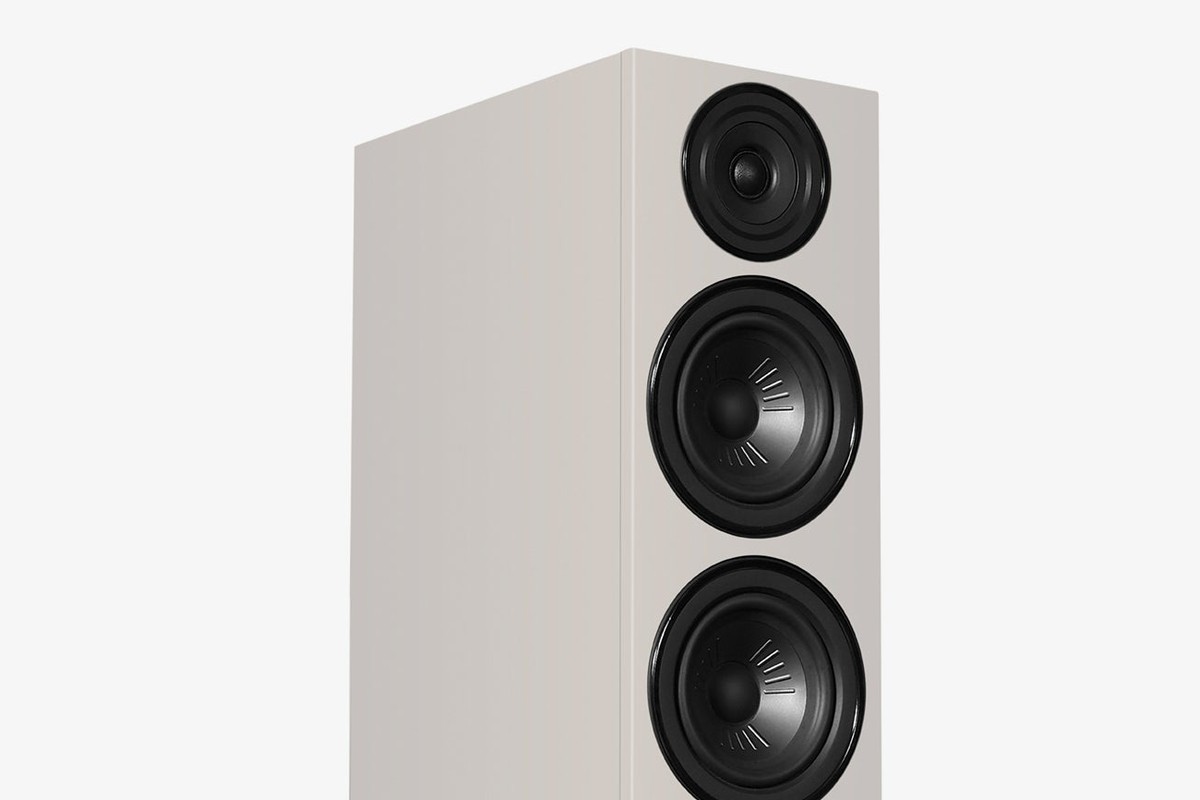 Grey speaker seen at three-quarter angle, with midbass cones and tweeter on the front