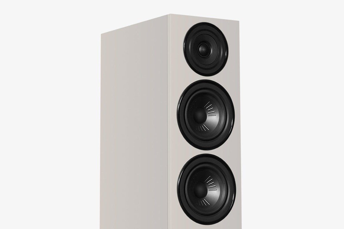 Grey speaker seen at three-quarter angle, with midbass cones and tweeter on the front