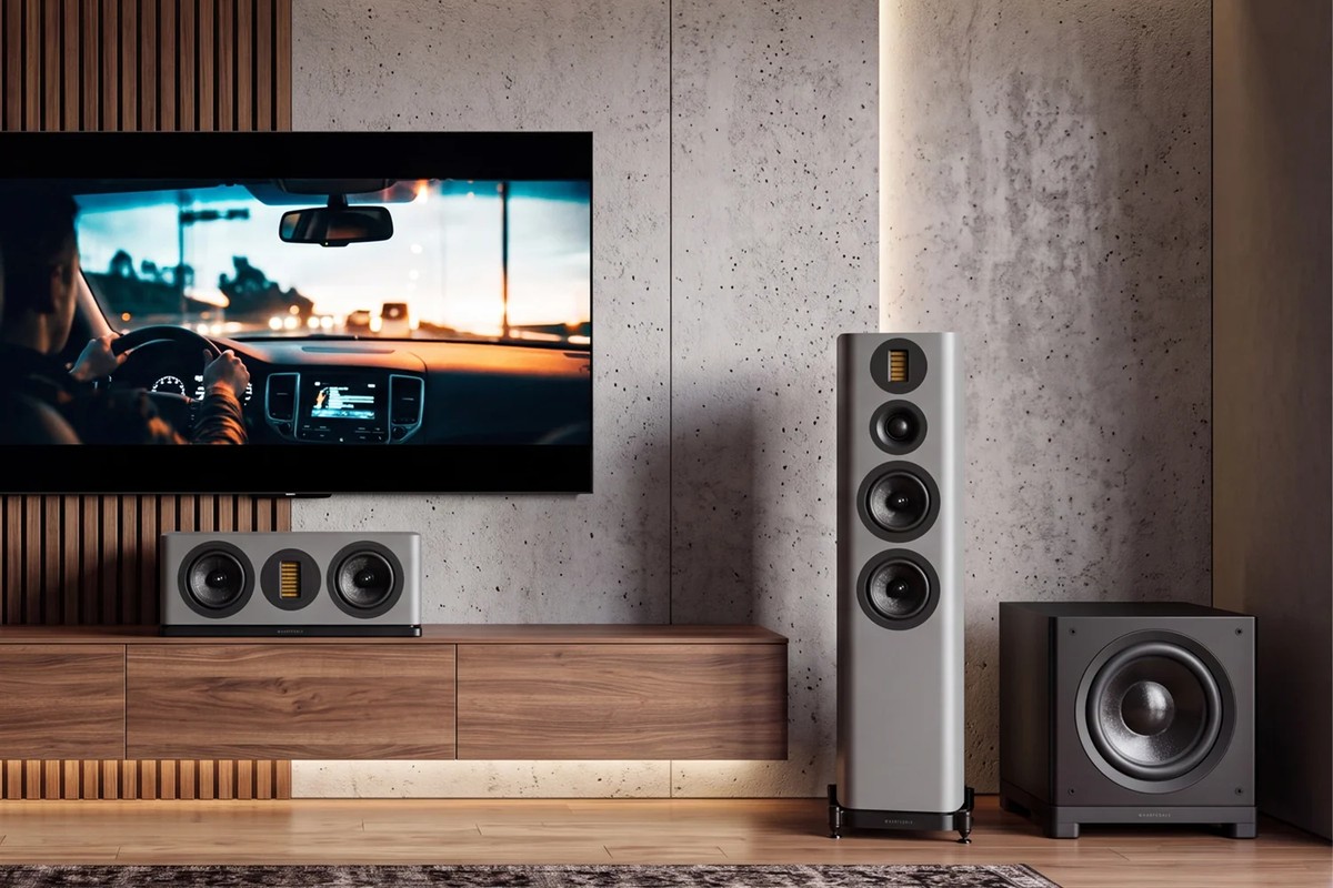 Living room with a wall-mounted TV, two grey floorstanding speakers, a centre speaker and the black subwoofer on the right