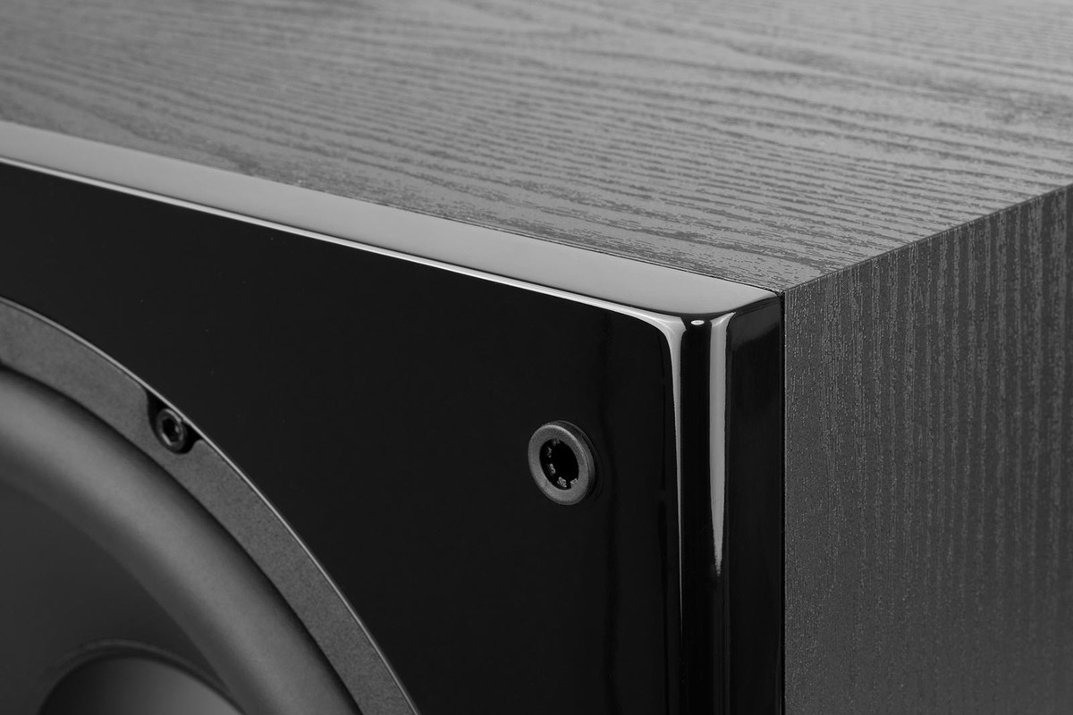 Corner of a black subwoofer: side in wood-grain vinyl and glossy front