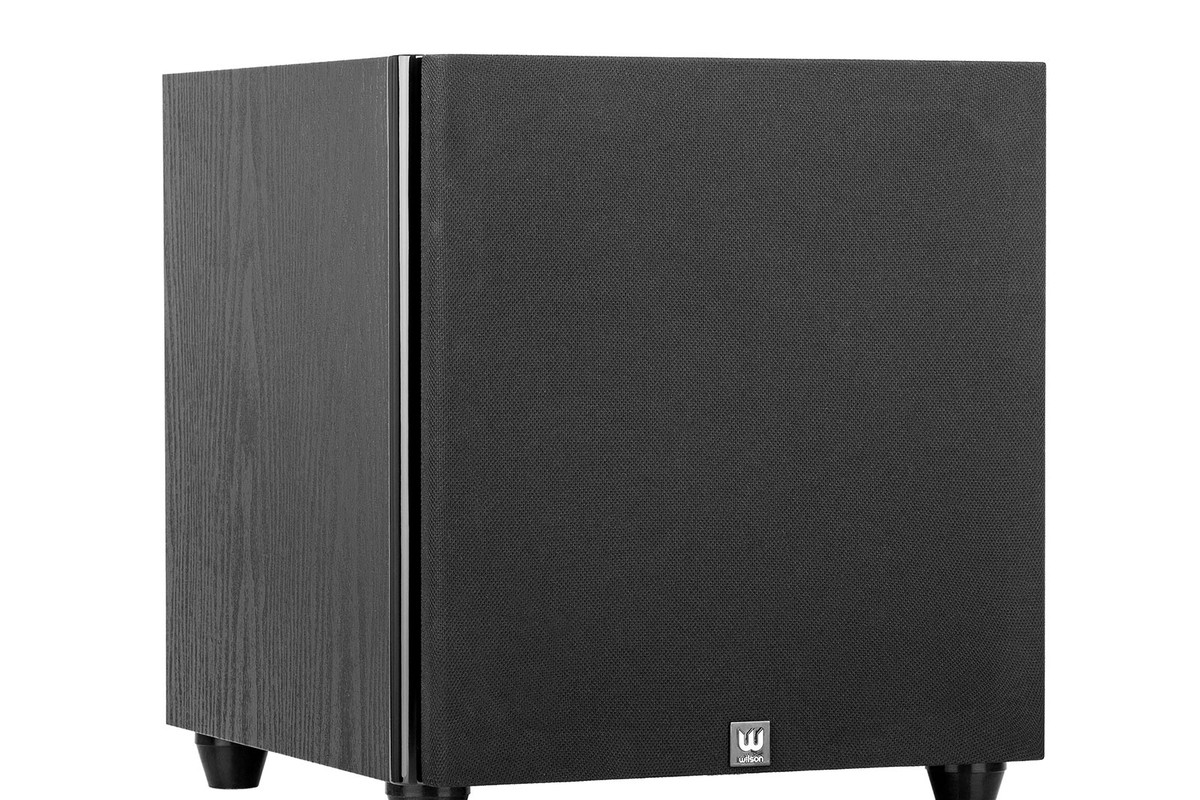 Black subwoofer seen from three quarters, front covered by a fabric grille