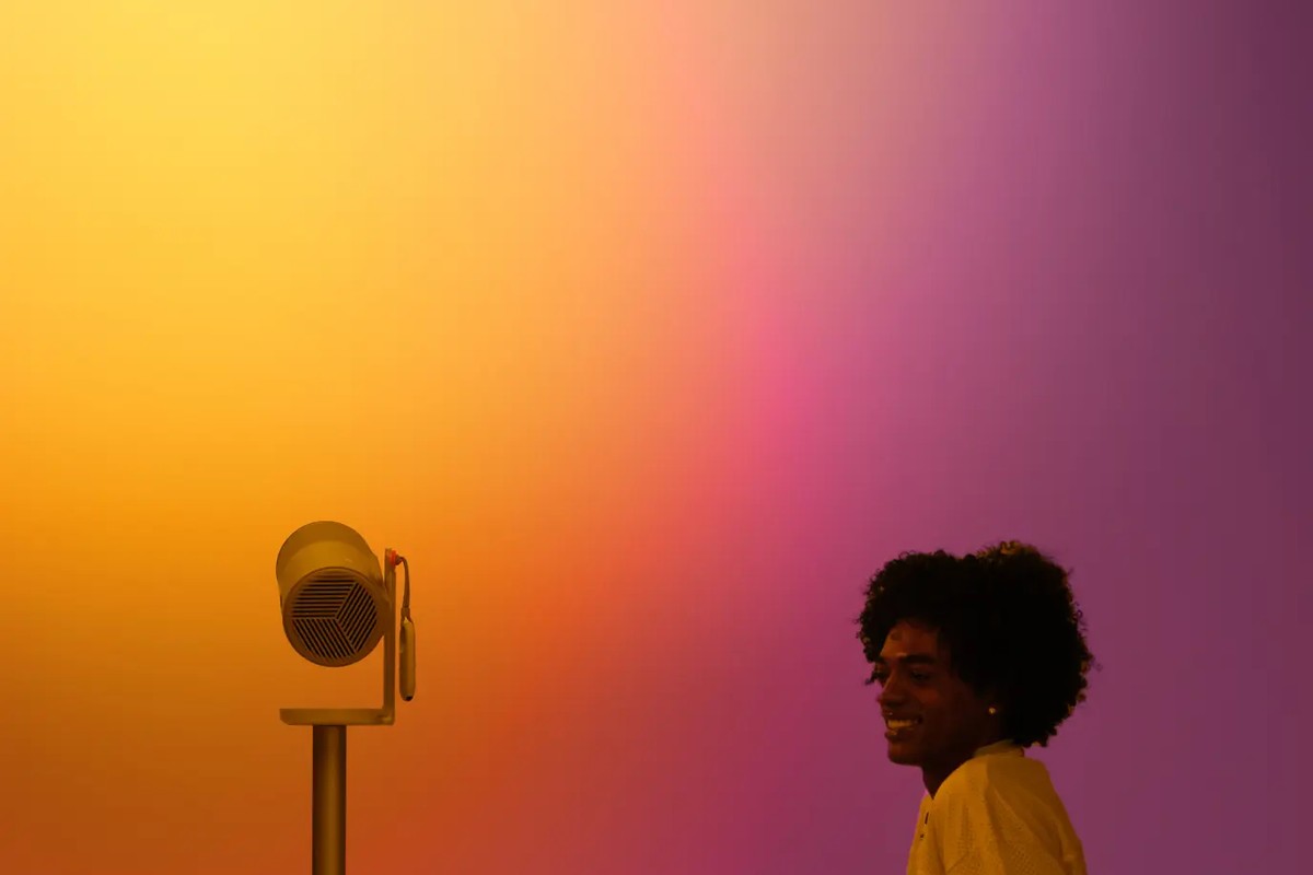 Petit projecteur sur pied dans une lumière jaune et rose, jeune femme souriante à côté