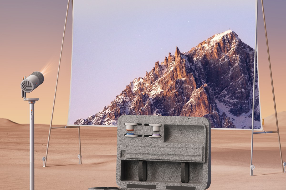 Proiettore su supporto davanti a uno schermo teso nel deserto, valigia da trasporto aperta in primo piano