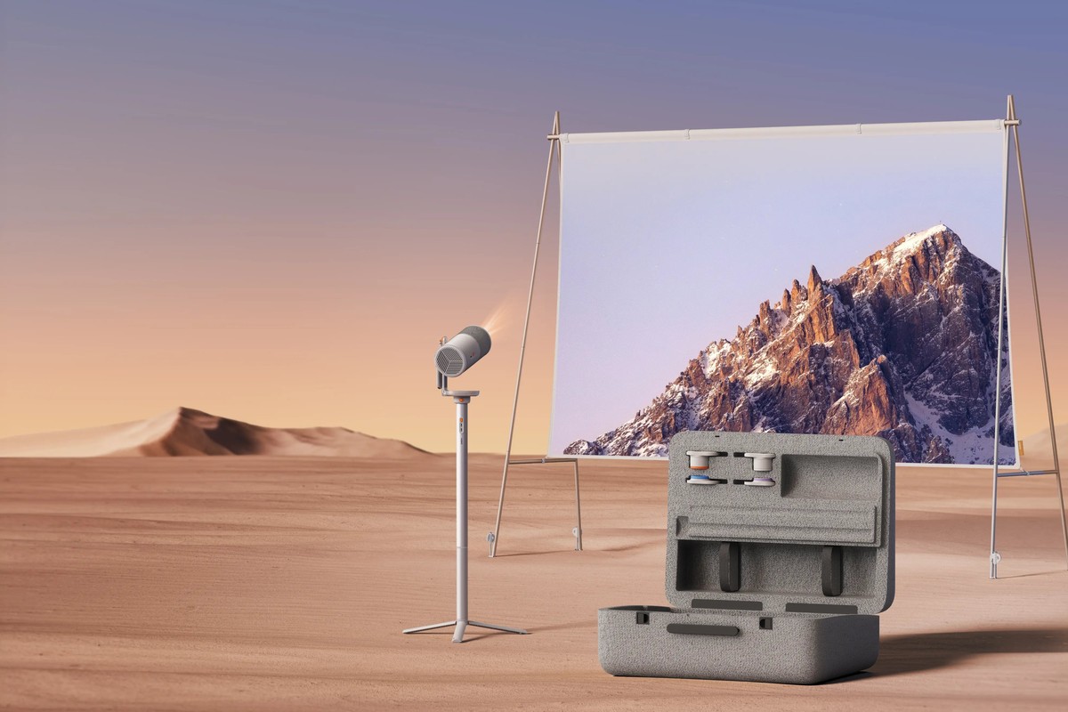 Projector on a stand facing a screen stretched out in the desert, open case in the foreground