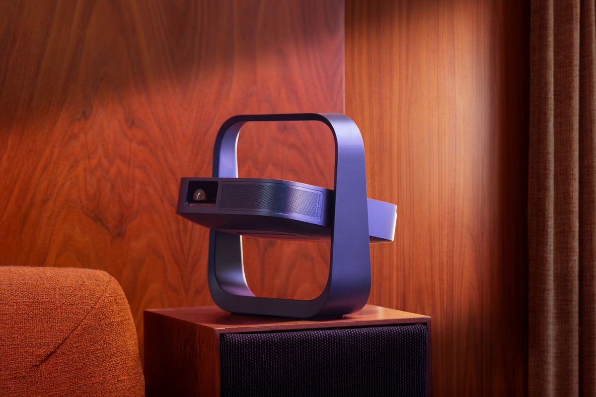 Petit projecteur violet à poignée posé sur un meuble en bois, à côté d'un fauteuil orange