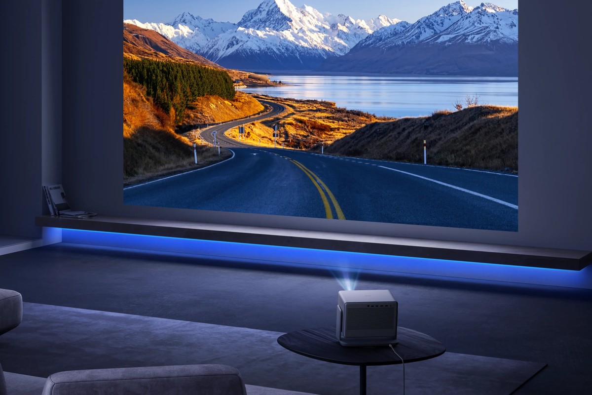 Grauer Beamer auf einem Couchtisch, Berglandschaft an der Wand eines abgedunkelten Wohnzimmers